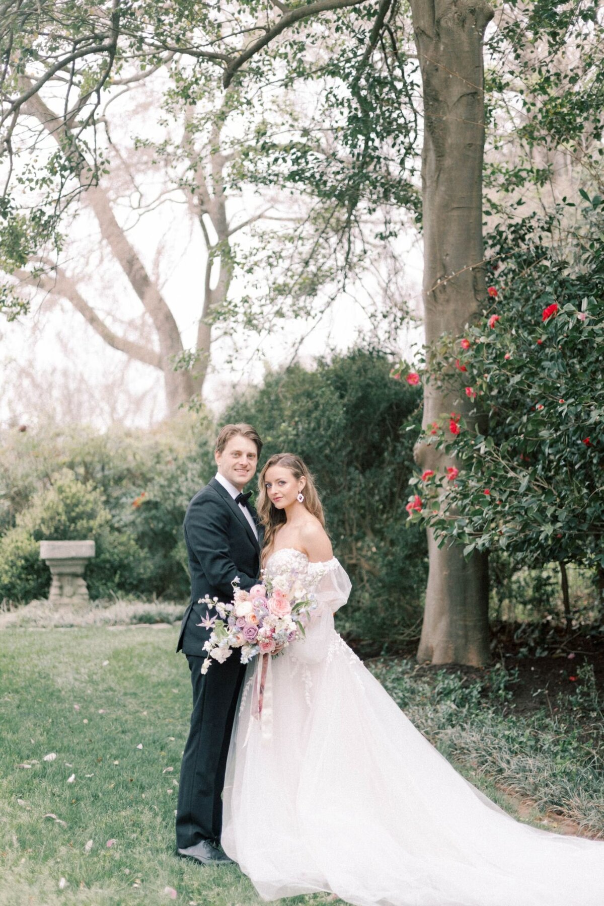 Bride and groom smiling in grass field with large trees.