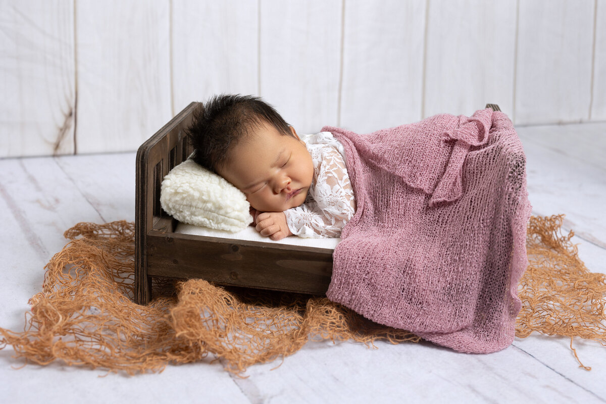 DMV - PhotobyShai -Newborn laying with her hand under her chin on a crib bed