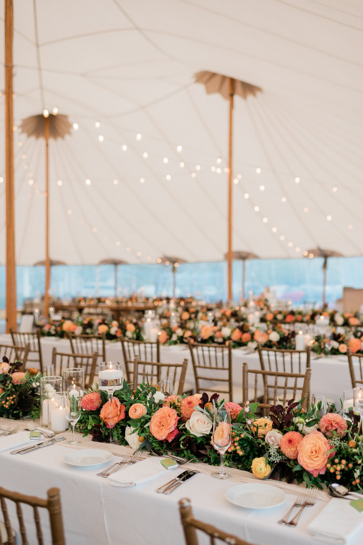 A wide-angle view of the wedding reception at Spring Lake Golf Club, with multiple long tables set under a tent illuminated by warm string lights.