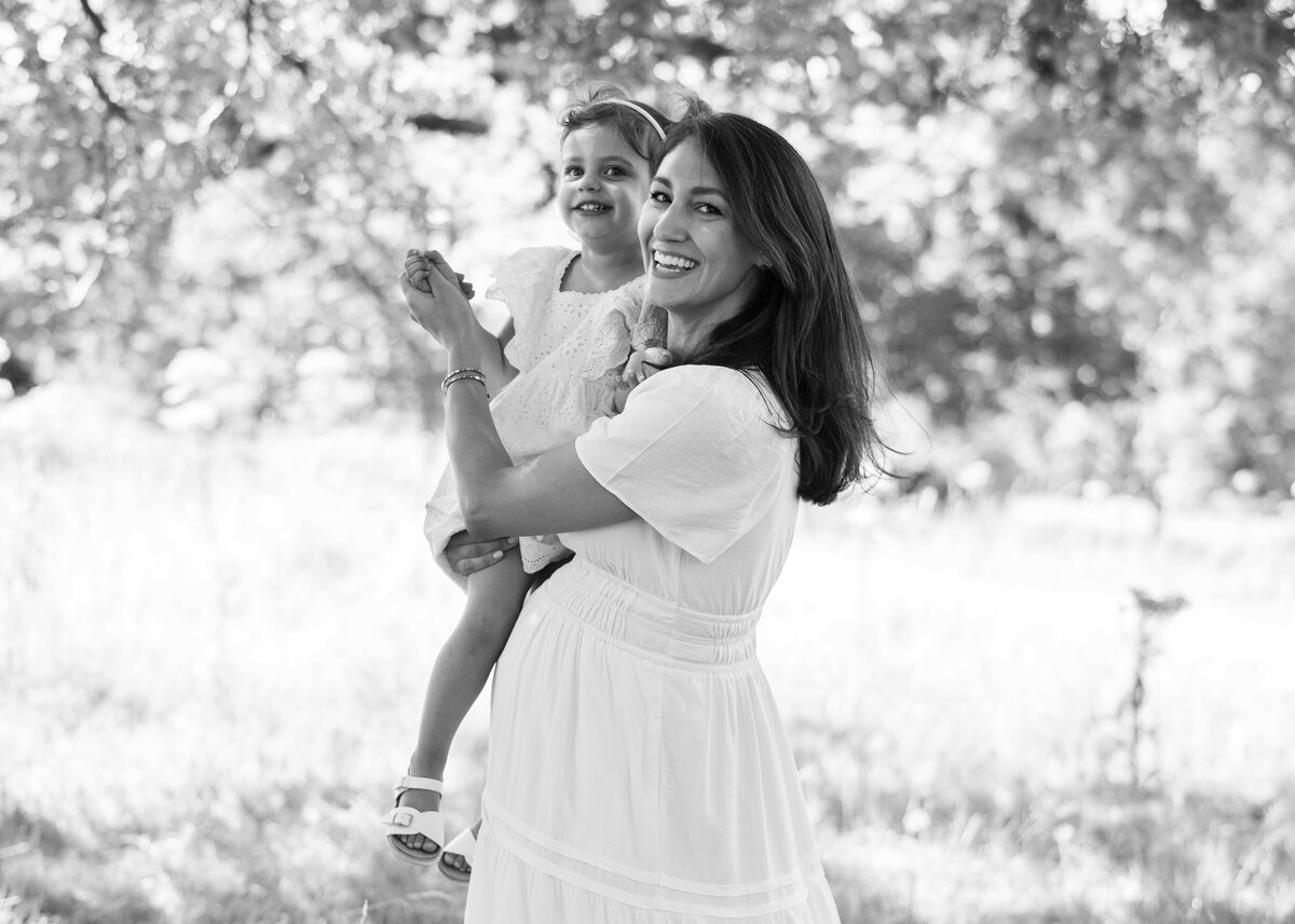 Motherhood photoshoot with pregnant mother and little girl dancing in park