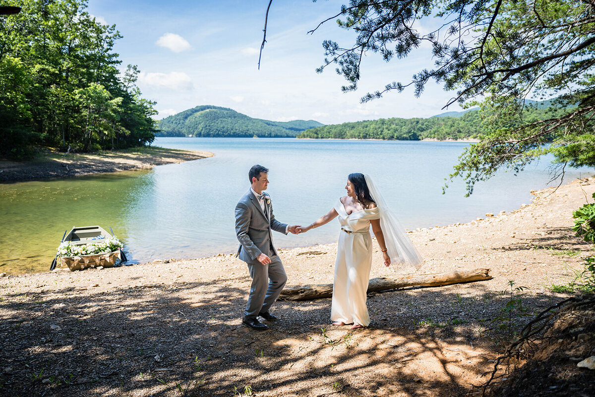 A couple on their elopement day in Roanoke, Virginia have their first dance along the shores of Carvin's Cove with a rowboat adorned in pastel flowers parked on the  shore.