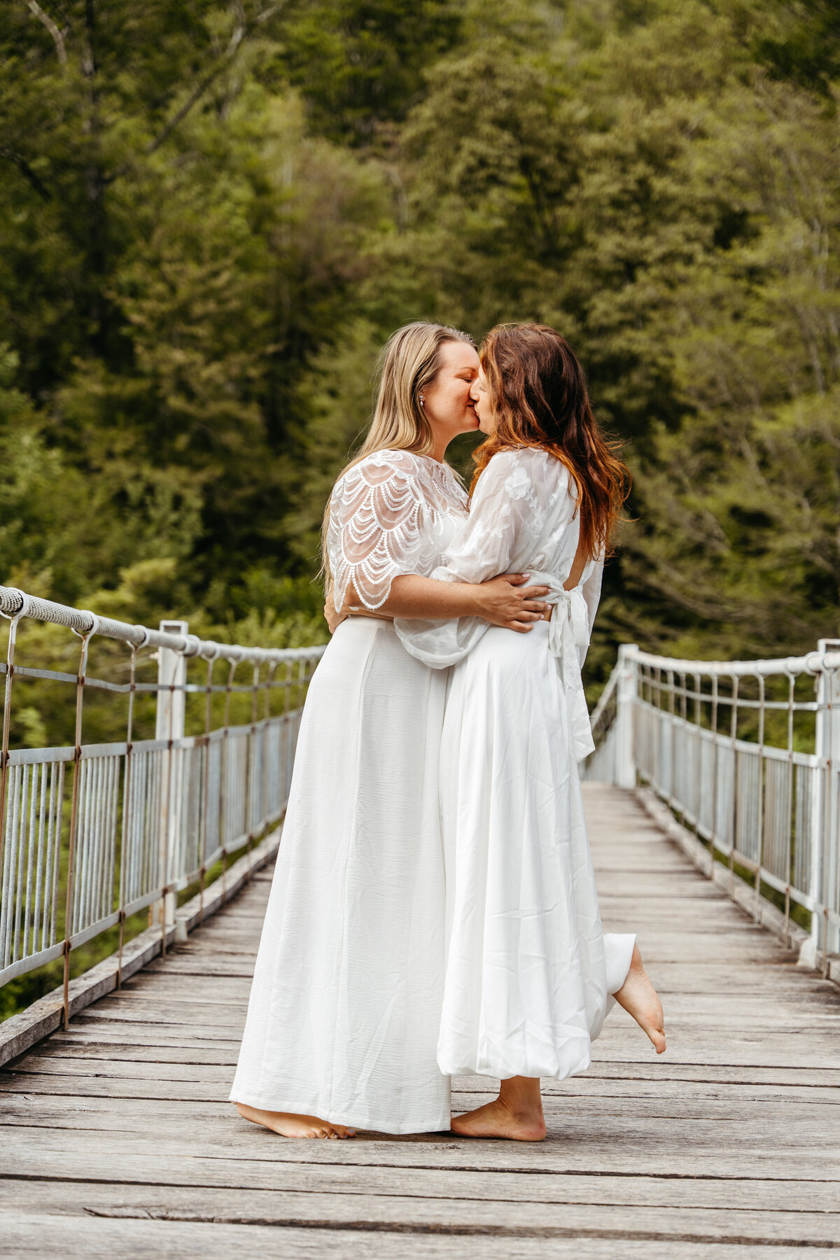 Same-sex elopement kiss on mountain river bridge