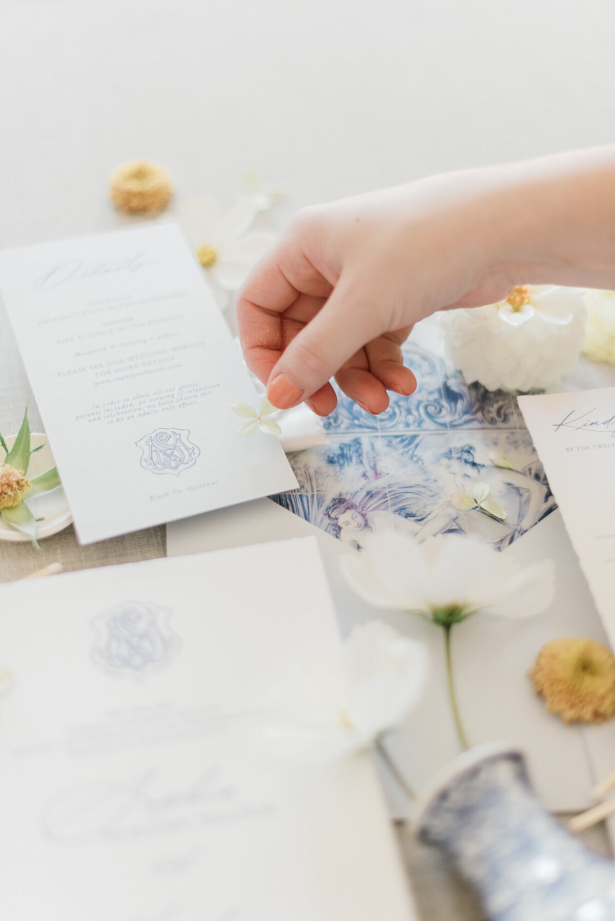 Wedding Stationery and details flatlay, styled by Wedding Stylist Rebekah Bronte, featuring blue and white details, navy ribbon, and yellow and white florals. 