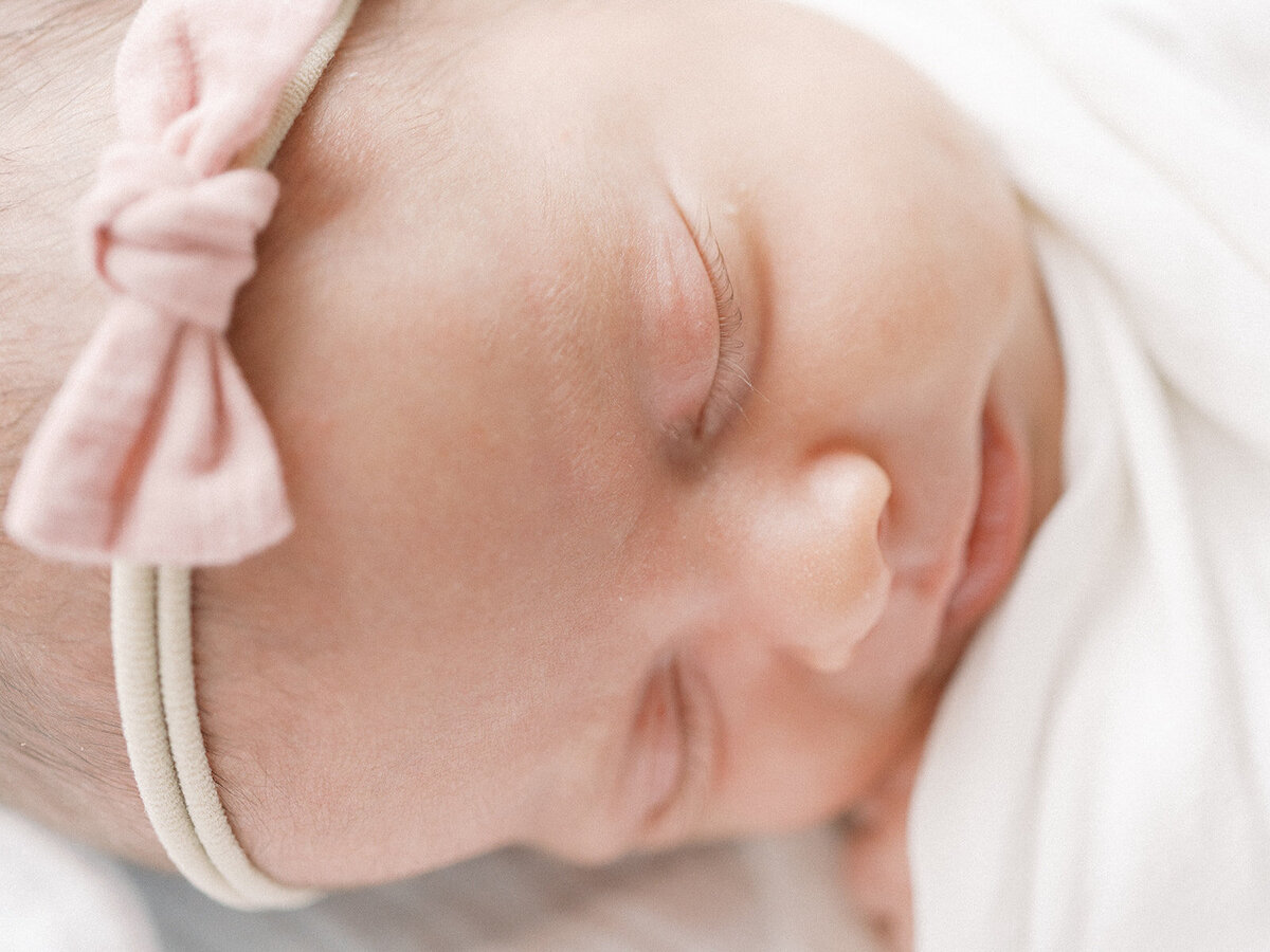 a close up of a newborn's face while sleeping and wearing a pink bow headband