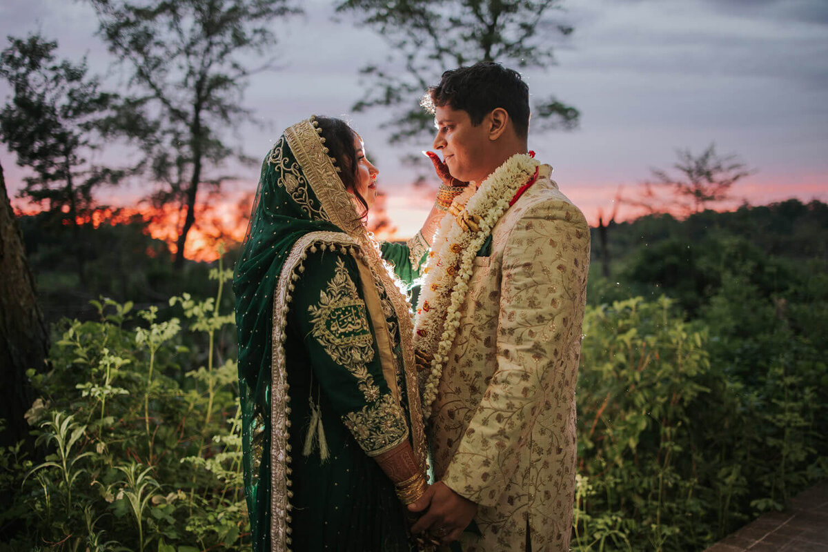 A couple shares a tender moment at sunset, with lush greenery in Princeton, NJ, enhancing the serene atmosphere.