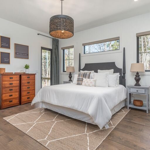 A master bedroom with hardwood floors and a white bed built by Mountain Legacy Builders in Asheville