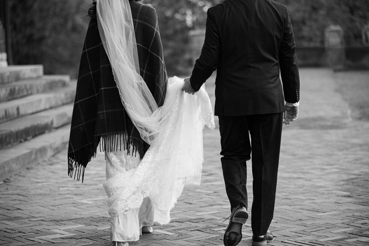 Groom holding brides dress as she walks along