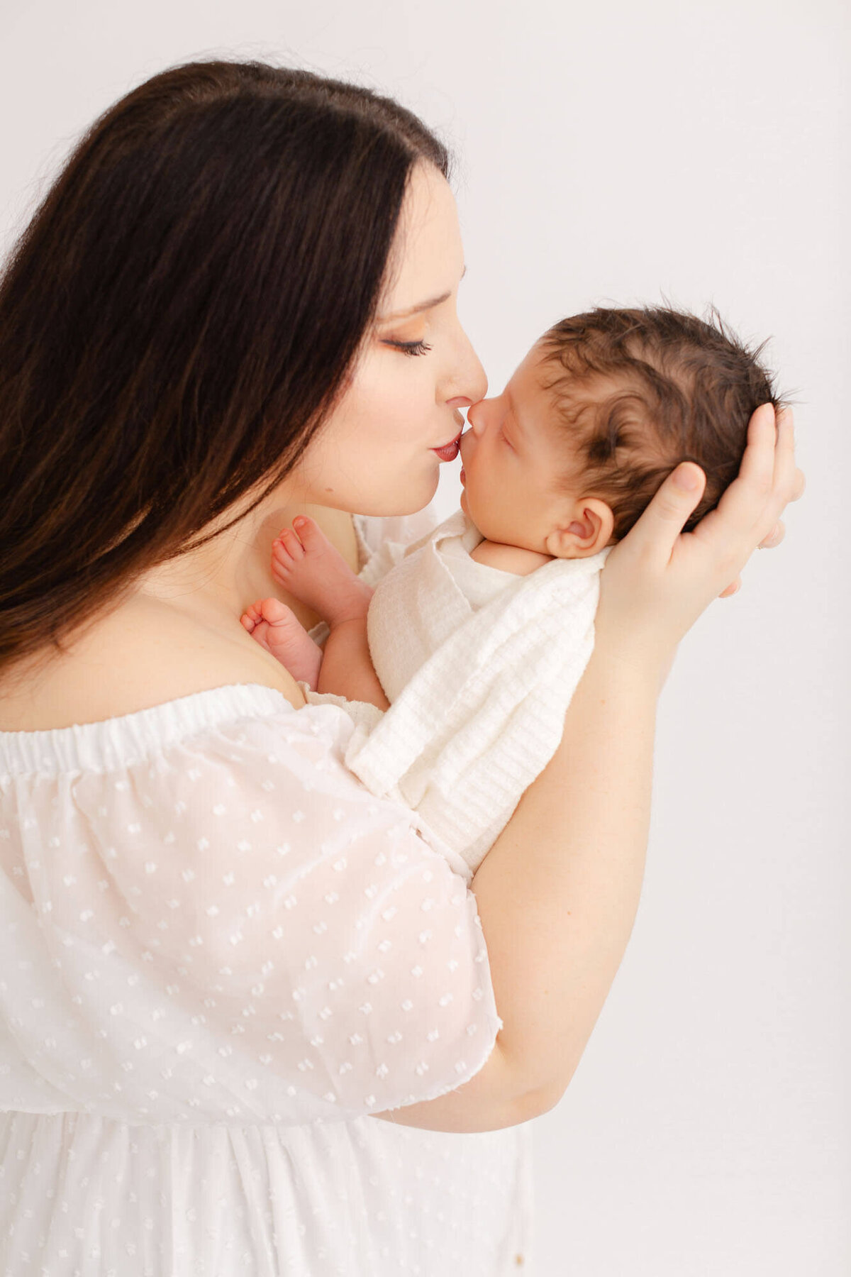 Mom in white dress kissing baby's nose at newborn photo session