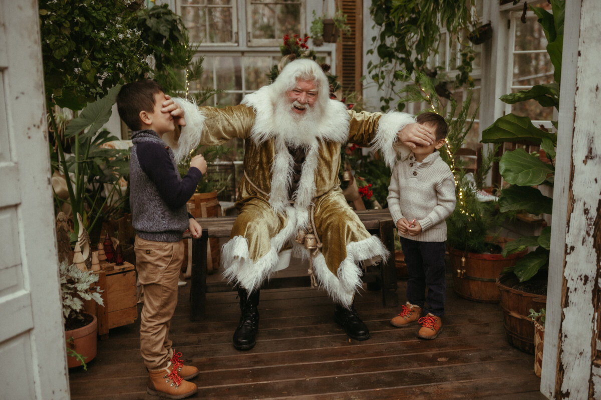 Santa holds his hands over two young boy's eyes at Das Hinterhaus. 