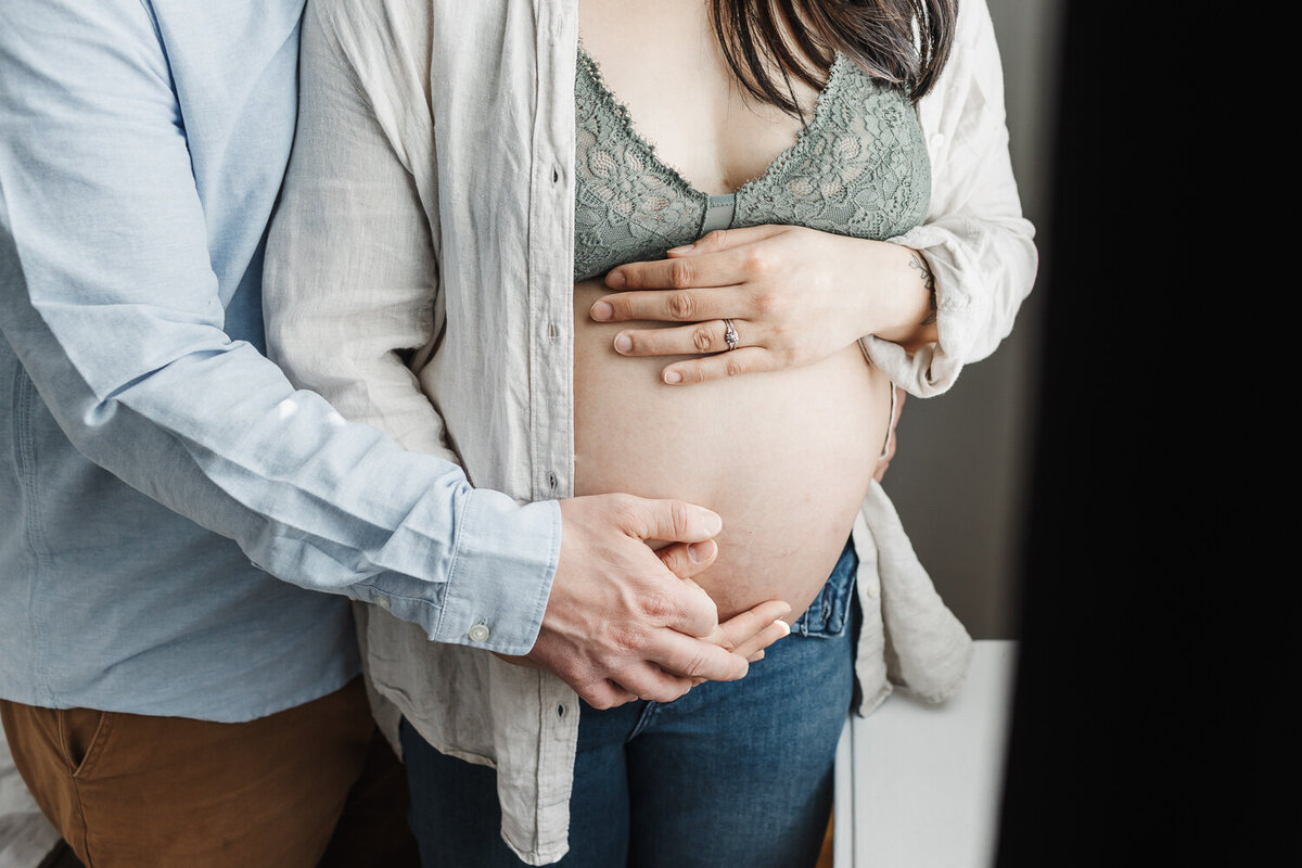 close up of pregnant womans belly with husbands hands lovingly holding it