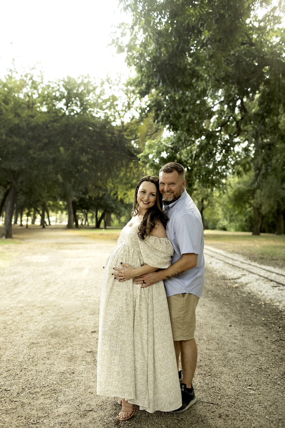 A beautiful maternity session at Trinity Park with mom and dad embracing each other, surrounded by lush greenery and a serene backdrop, captured by Chunky Monkey Photography.
