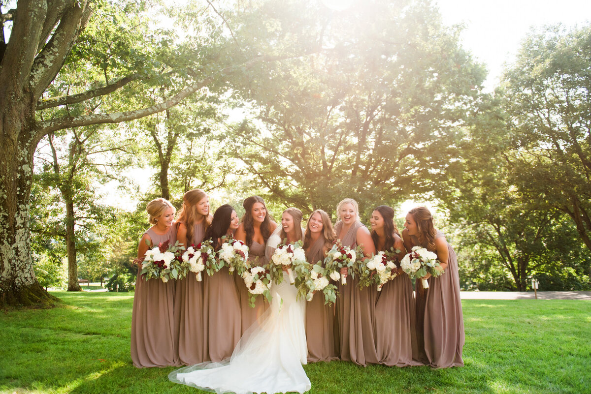 bride and bridesmaids posing for wedding pictures in the sunlight next to the mansion at oglebay resort