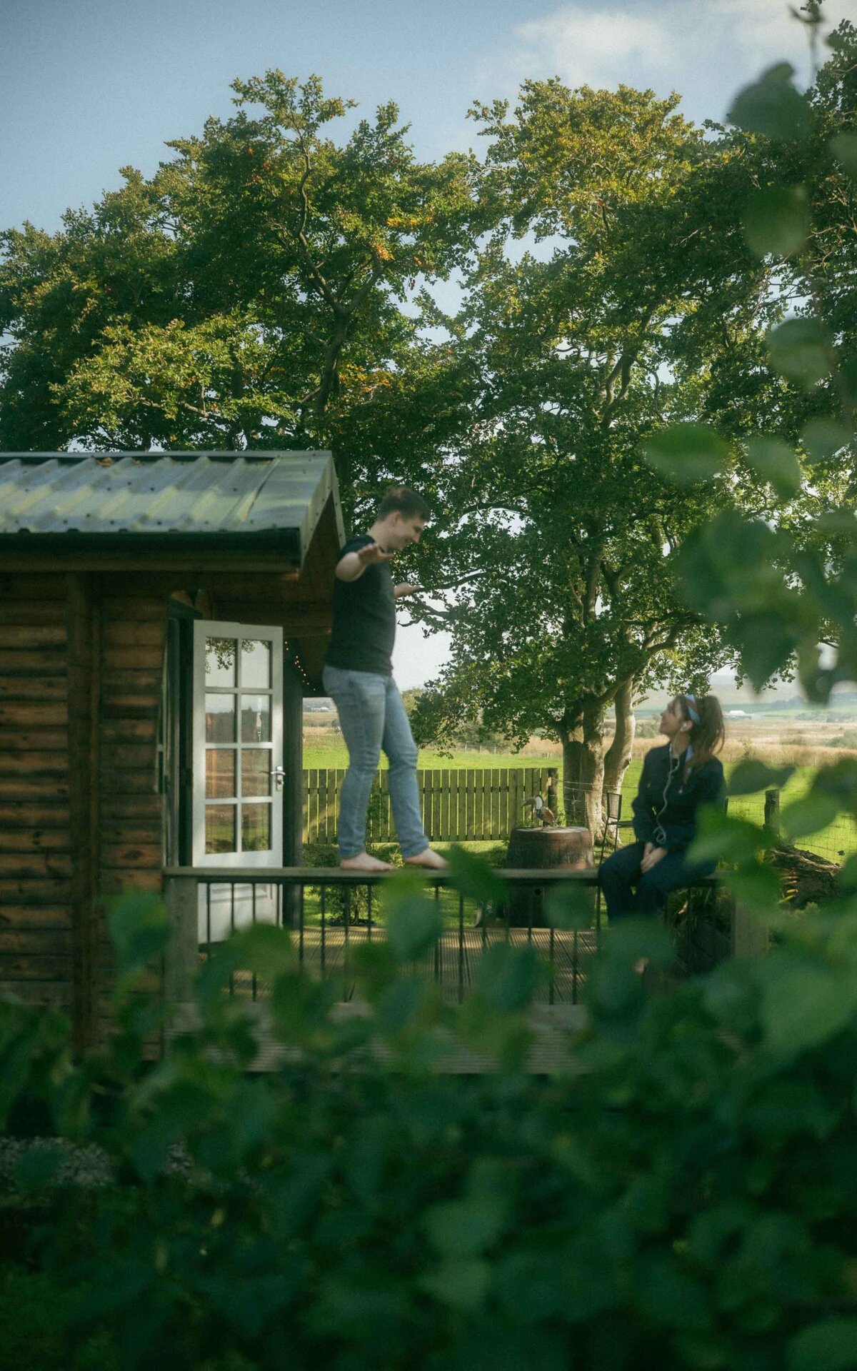 Capture the beauty of a couple photoshoot with the man walking on a charming porch, while the woman gazes at him lovingly. This intimate moment, set against a scenic porch backdrop, showcases effortless romance and connection