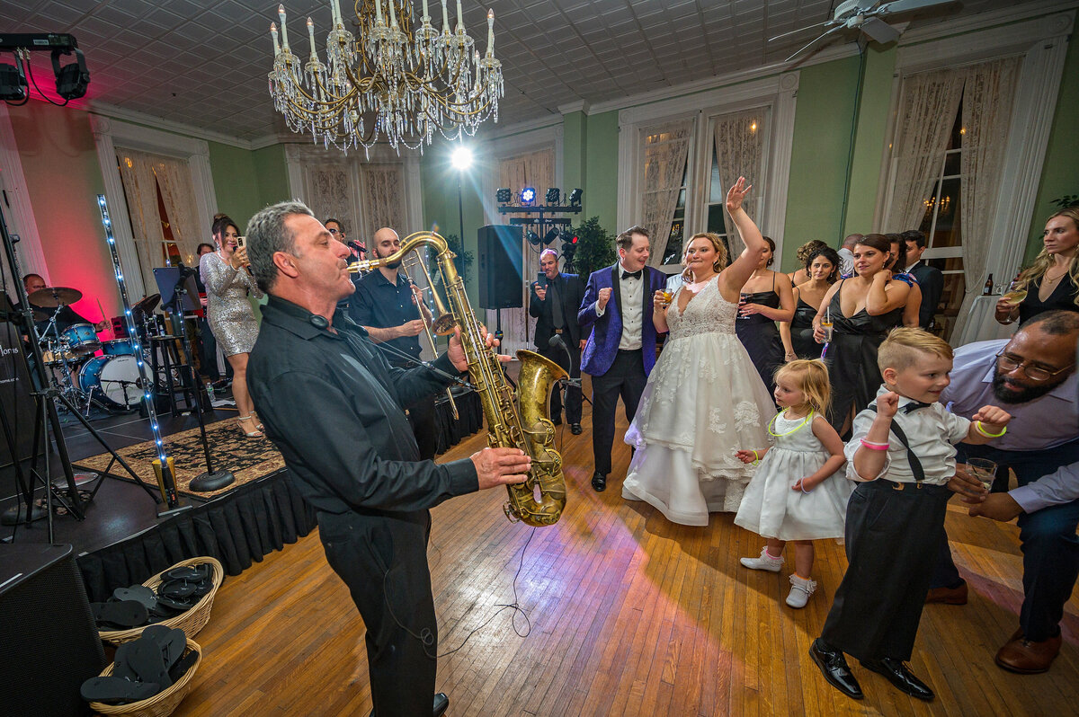 Man playing saxophone at a wedding while bride and groom dance.