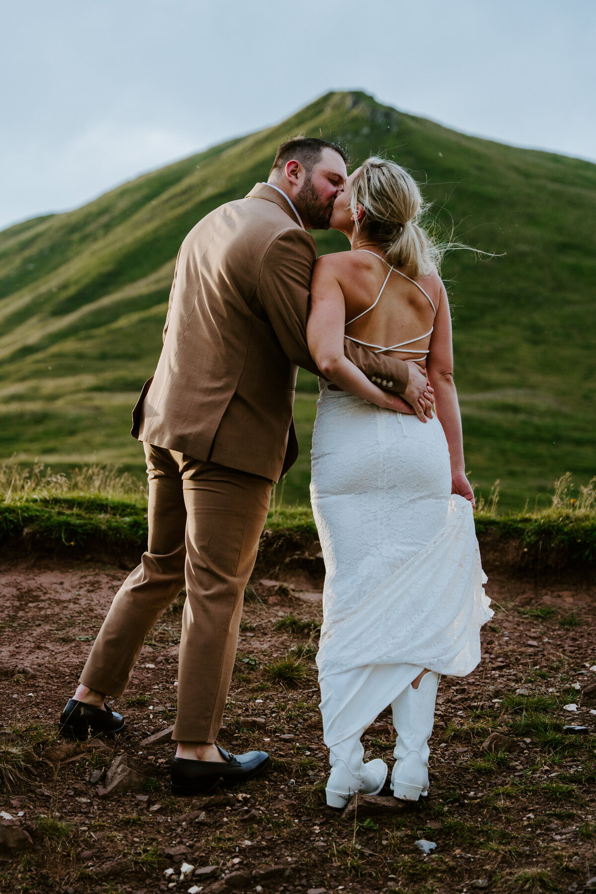 Bride lifting dress hem while walking on rocky trail