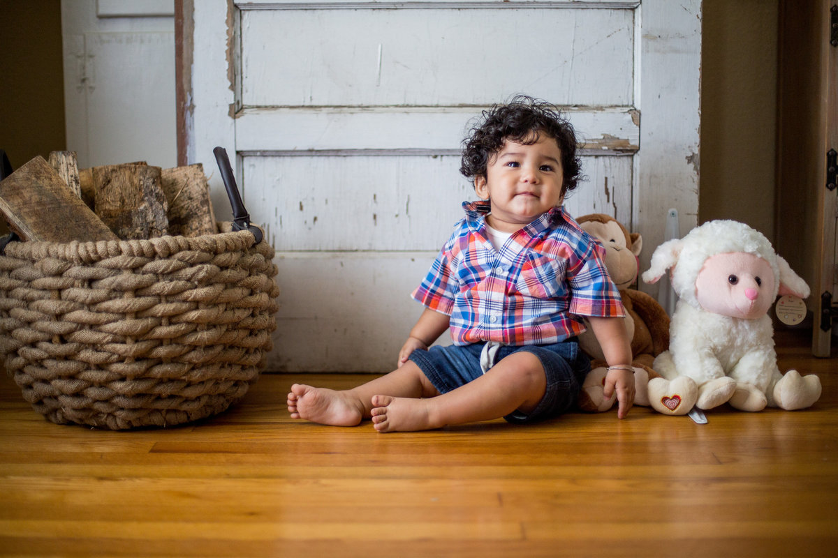Baby sitting on wood floor in front of a door and with lamb prop next to him.