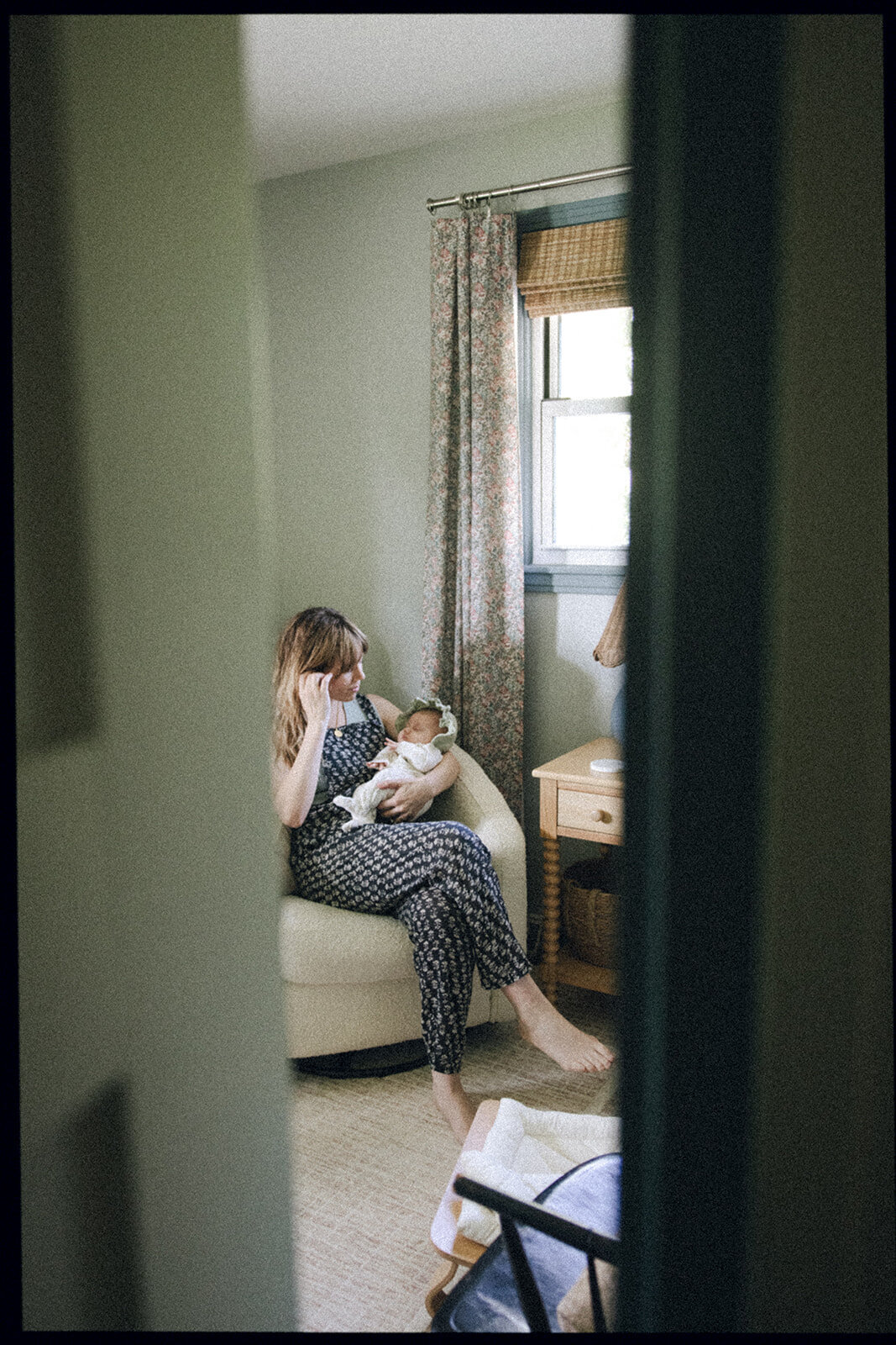 Mother holds newborn baby in baby's new room while brushing back a strand of her hair.