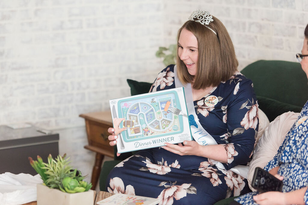 Mom-to-be joyfully opening gifts at a woodland-themed baby boy shower.