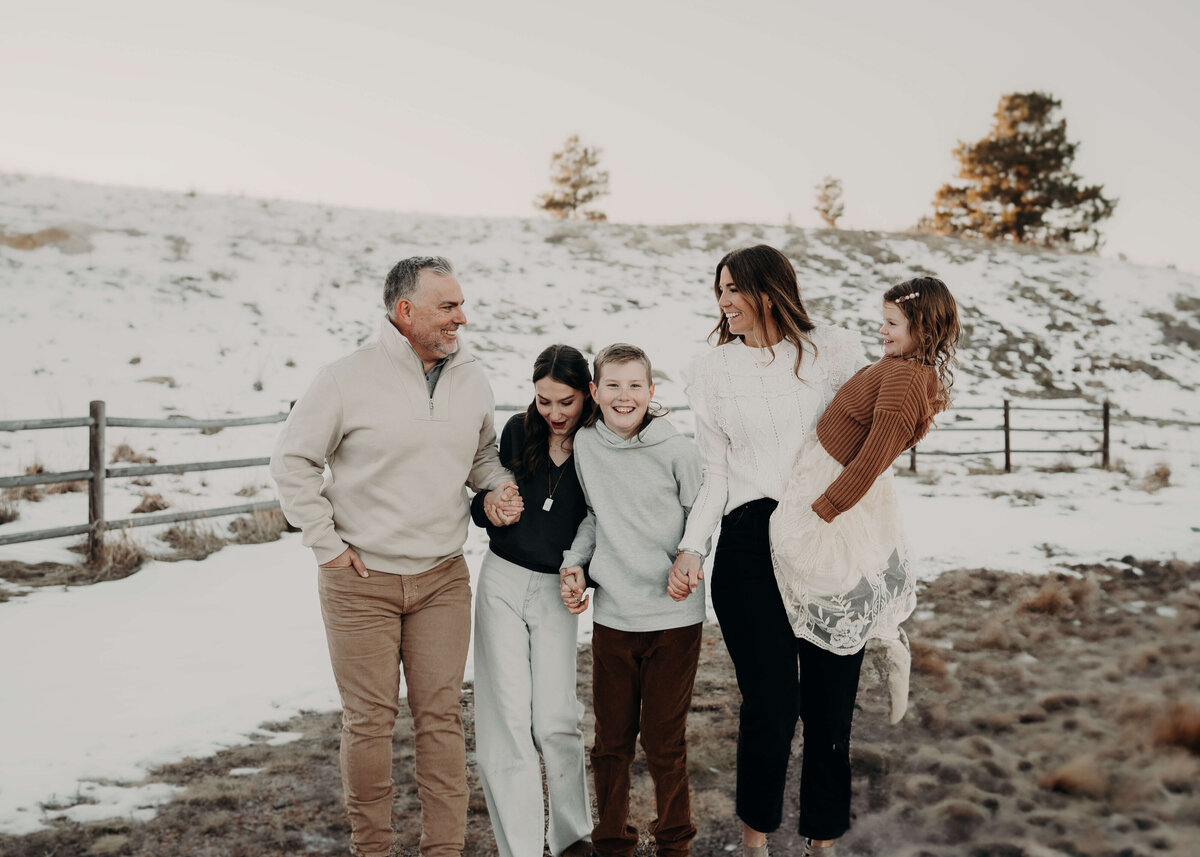 A family of five walks on a trail, surrounded by beautiful snowy hills and a gorgeous old fence, while dressed fashionably in Brown's and creams to coordinate with the winter backdrop.