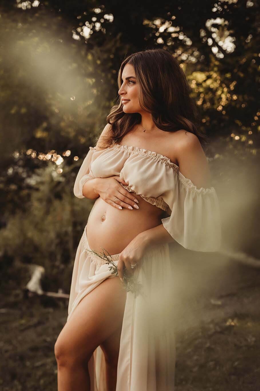 A pregnant mother in a powerful stance holding her bump whiling gazing in the distance