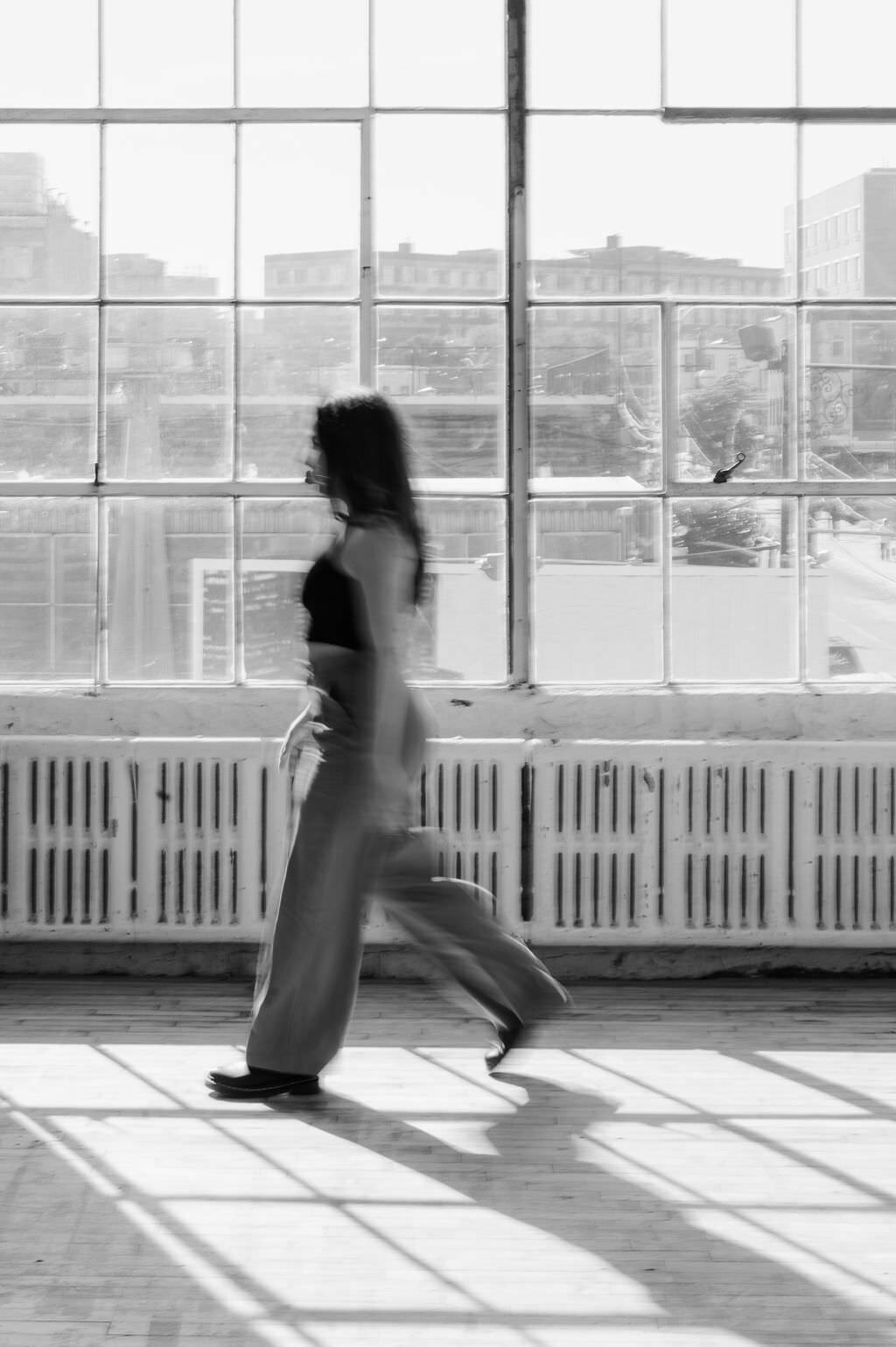 blurred black and white photo of a woman walking along a window
