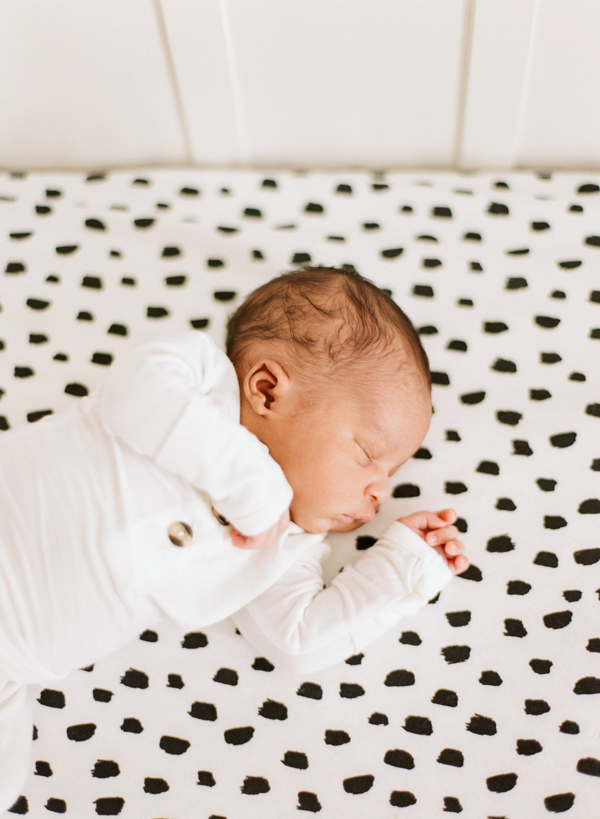 Baby lays on a black and white polka dot crip sheet while sleeping during a Raleigh NC newborn photography session. Photographed by newborn photographers Raleigh A.J. Dunlap Photography.