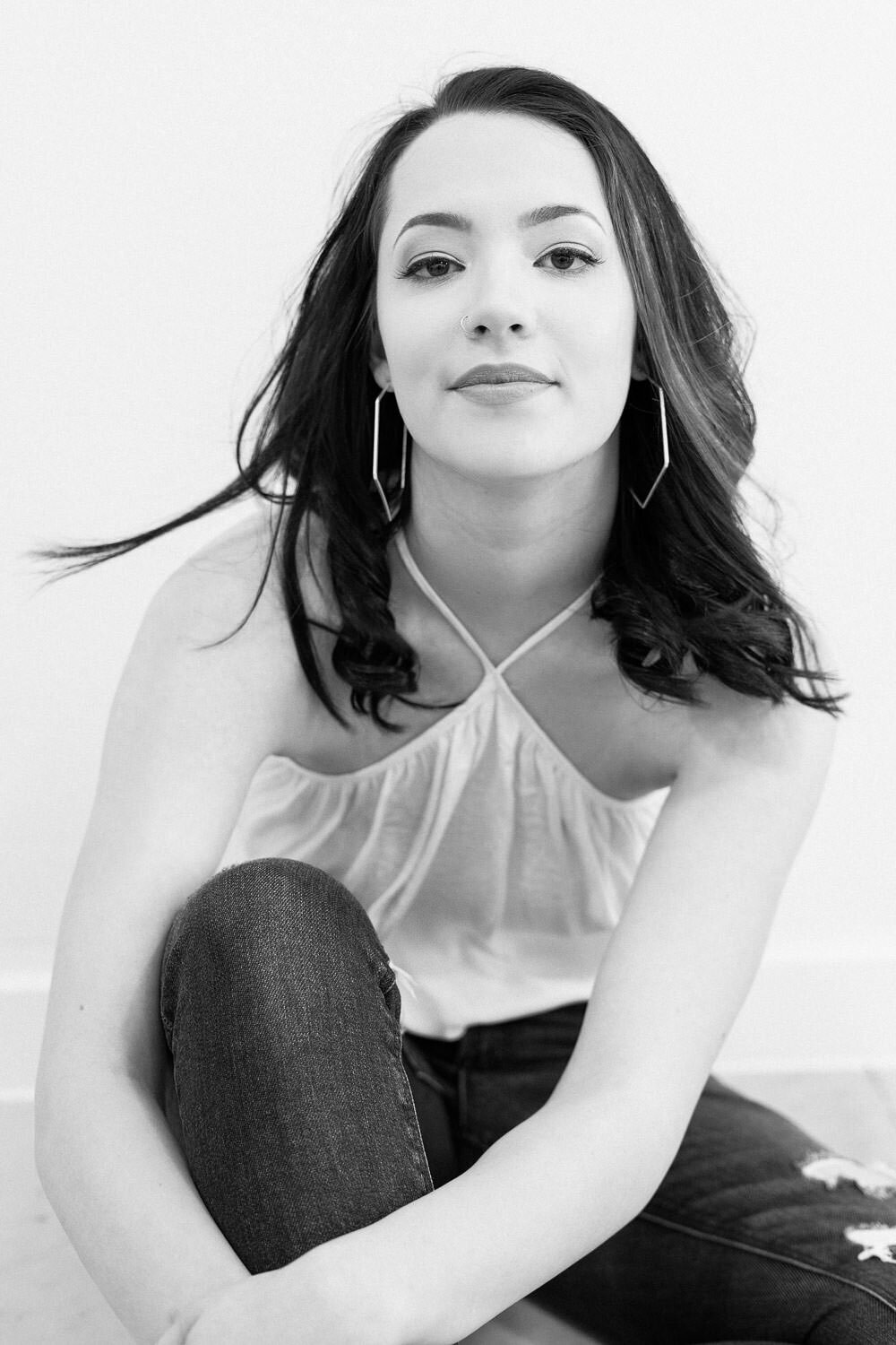 Editorial-style headshot of a confident woman seated on the floor against a white wall in Austin, TX