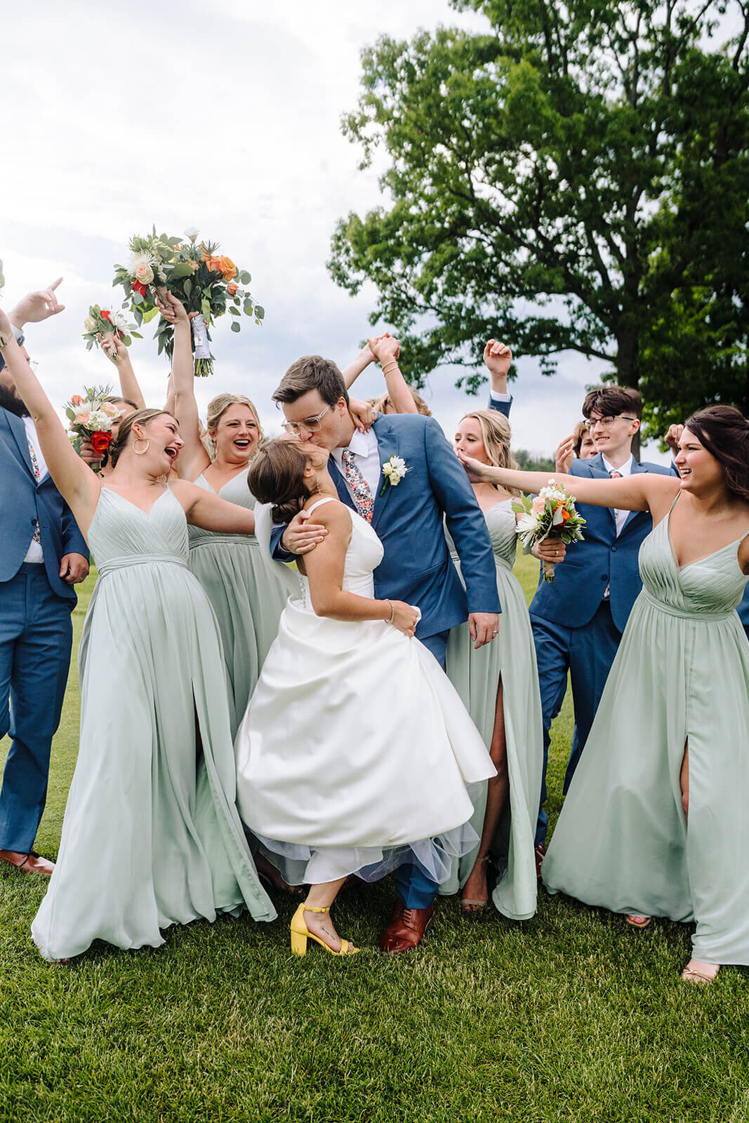 Bride and groom kissing as wedding party cheer at Oswego wedding, NY