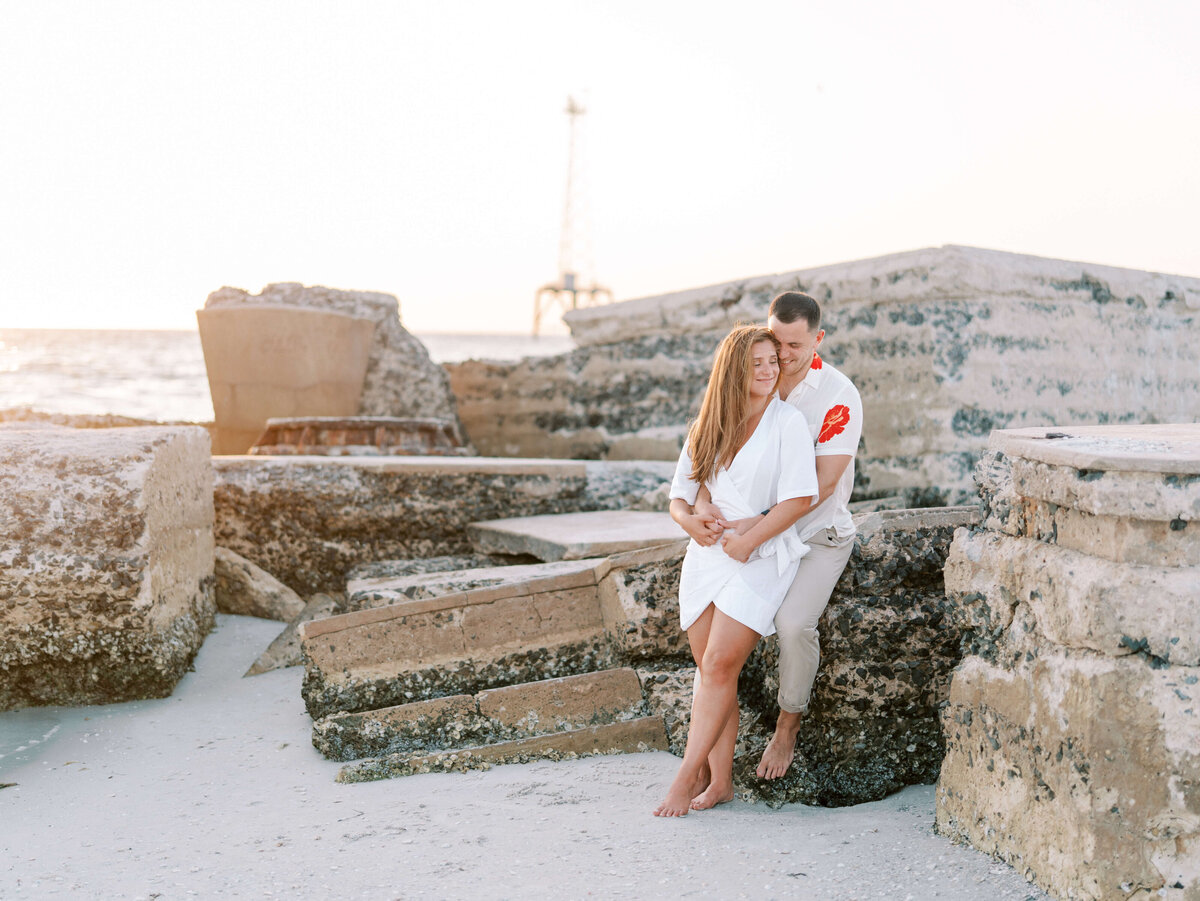 Couple standing on rocky beach in Fort De Soto with ocean sunset behind them