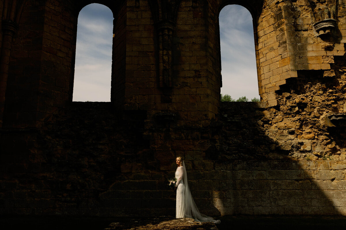 Bride stood in a shaft of sunlight in the ruins of Byland Abbey