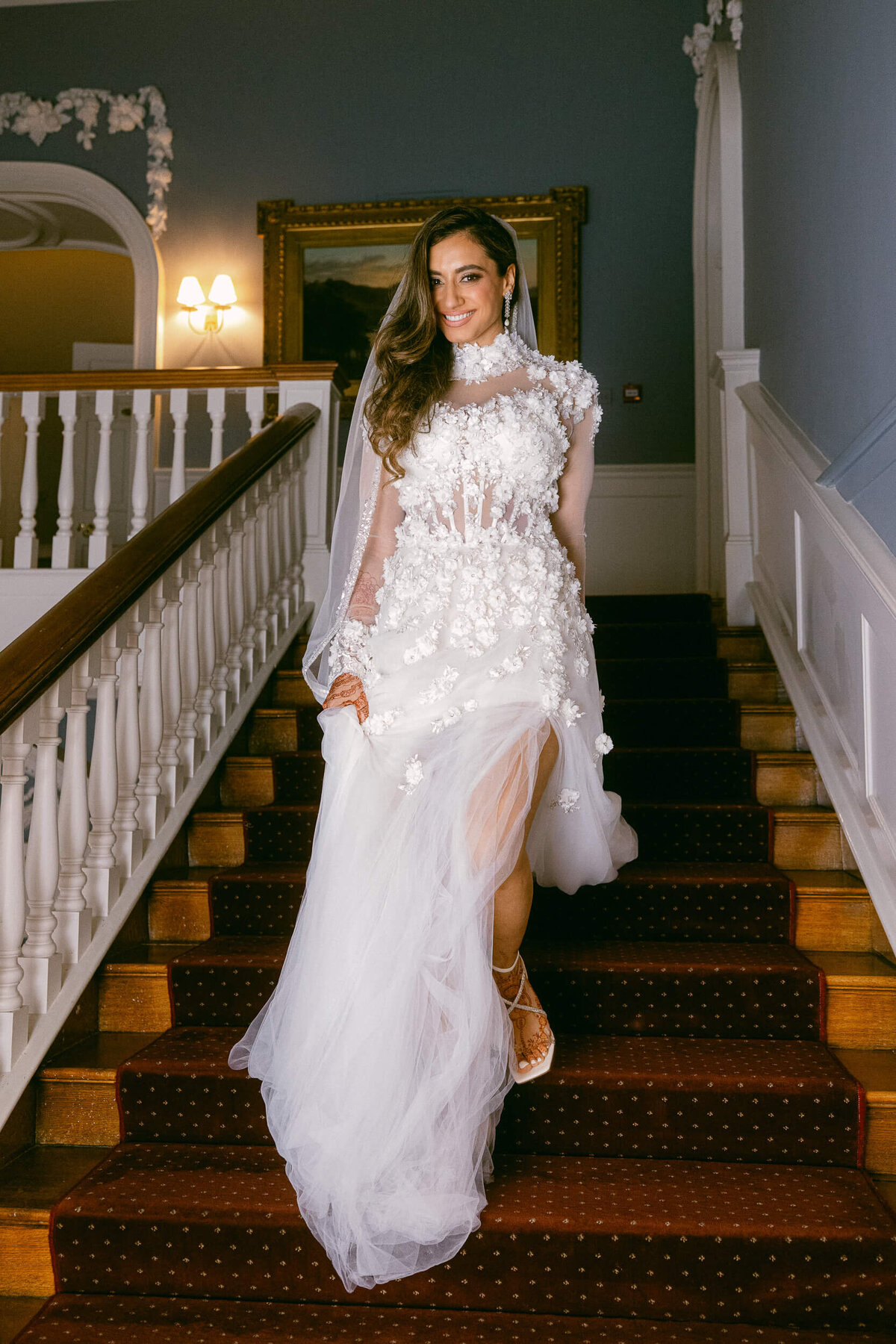 A wedding photo of the bride walking down a staircase in her white wedding dress