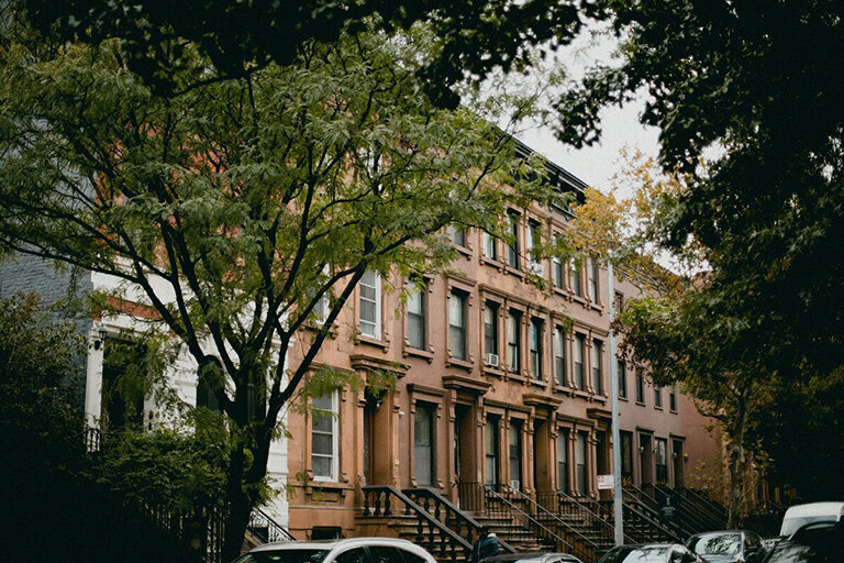  A row of brown brick buildings with cars parked along the street under a clear blue sky.