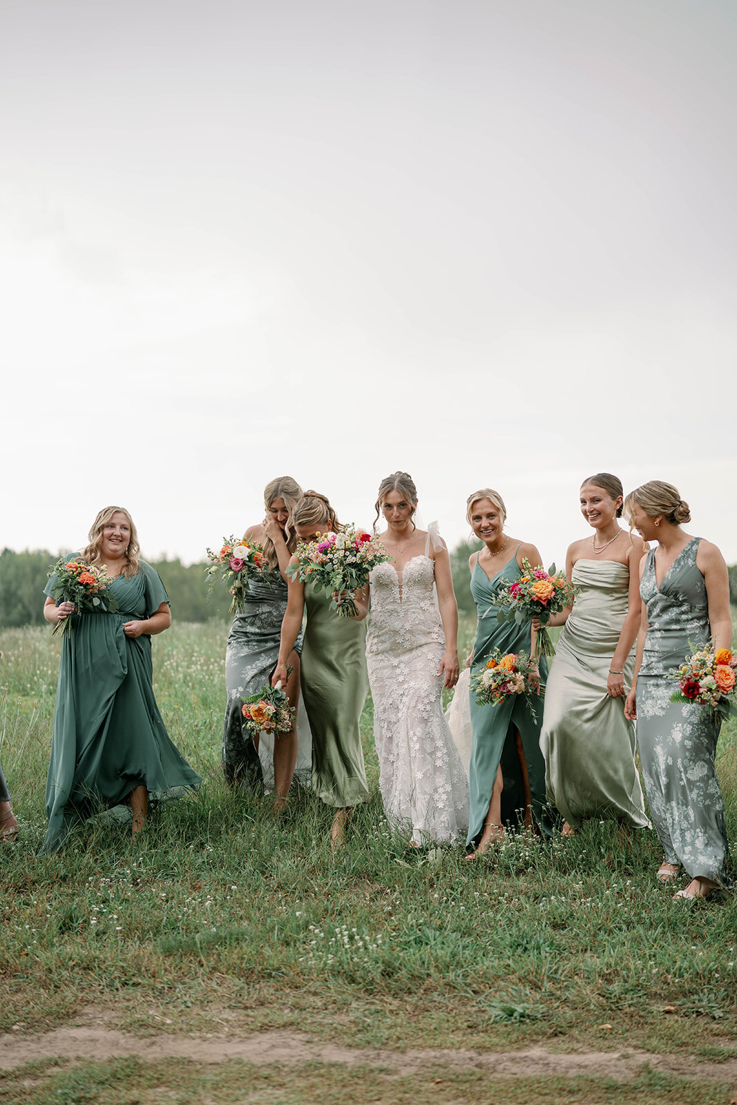 Bridesmaids standing together in sage green and floral dresses during a September orchard wedding at Nugent Orchards in Frankfort, Michigan.