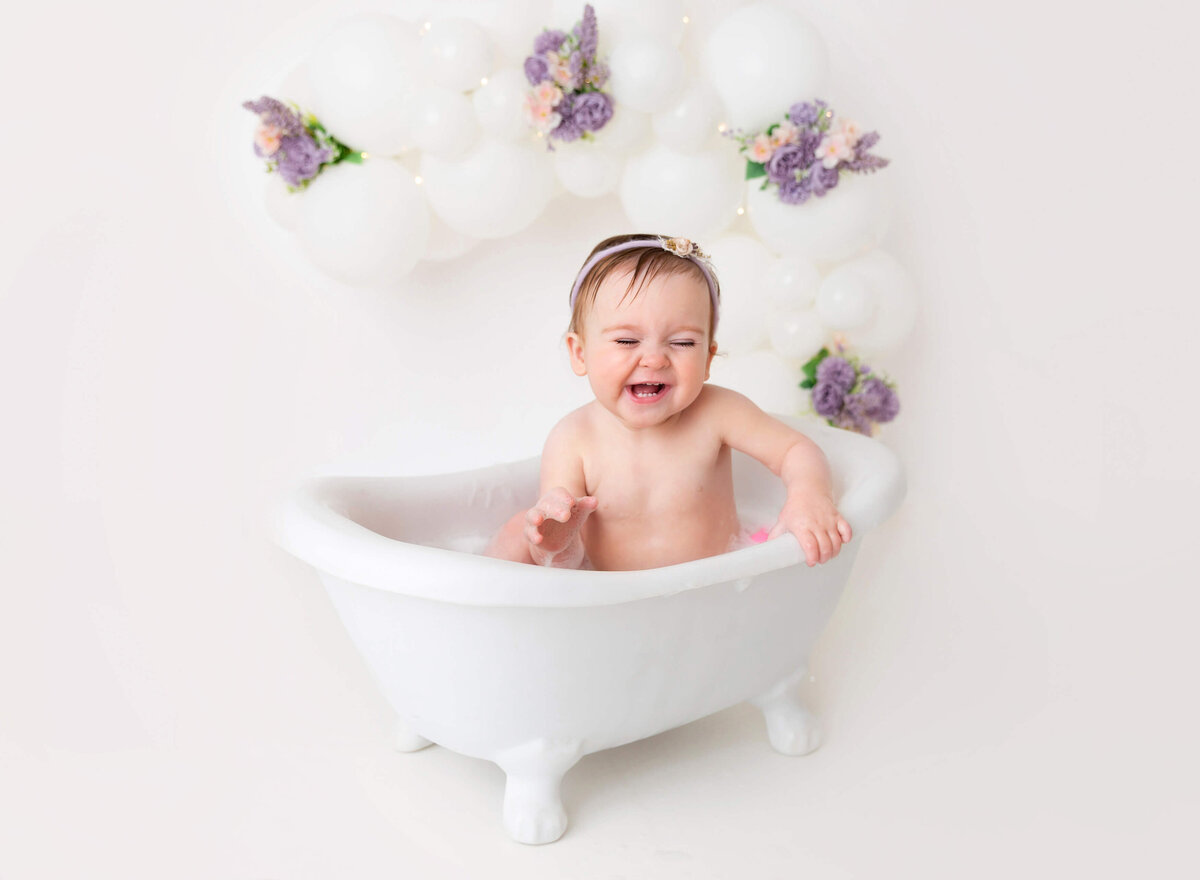 A baby girl enjoys a bubbly bath during her Brooklyn cake smash photoshoot, capturing the joy and innocence of her special moments in a timeless and playful setting.