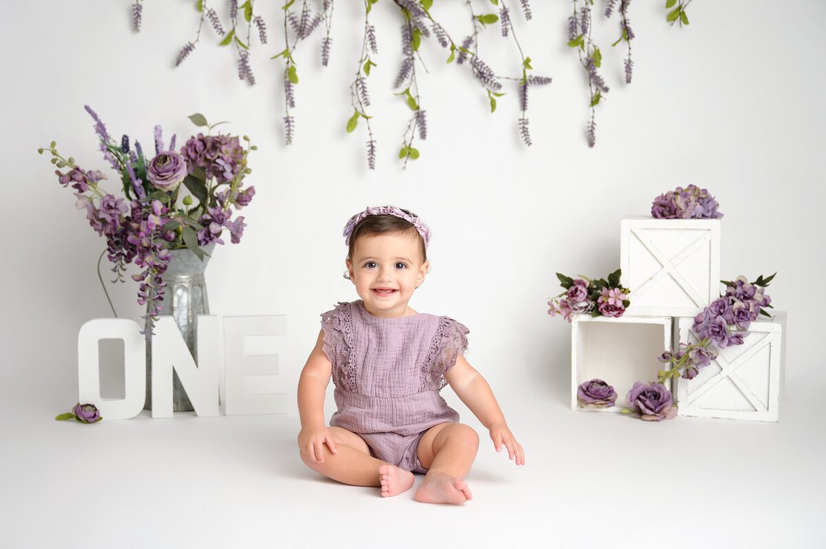 One Year Old Poses for purple flower cake smash photography session in West Palm Beach.