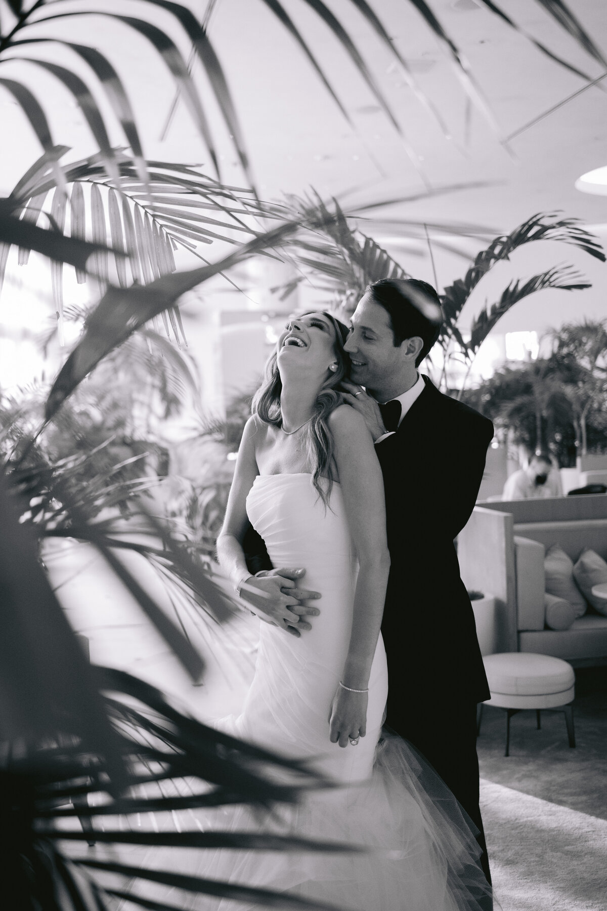 Bride and groom laughing together surrounded by tropical palm leaves, photographed by Rodrigo Varela Photography.