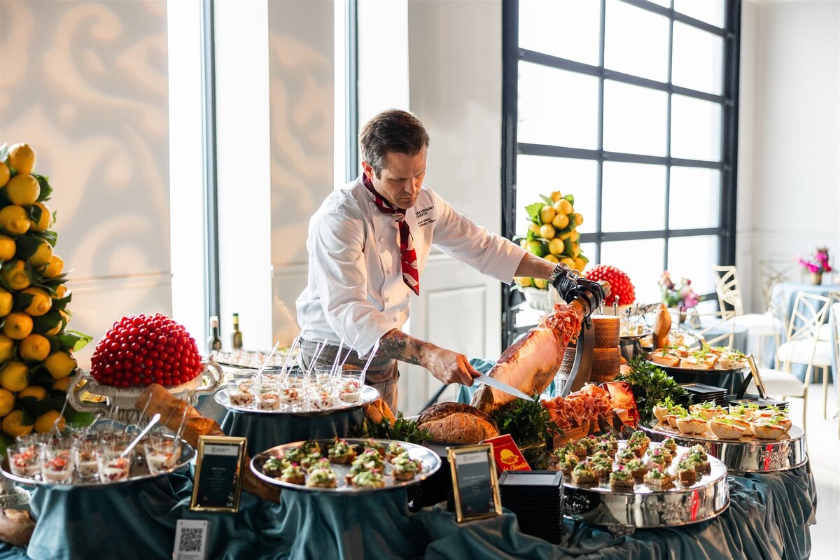 Venue space set up as spanish-inspired food station, with neatly arranged bite sized food filled with gourmet toppings on elegant platters, displayed on a styled table with decorative accents