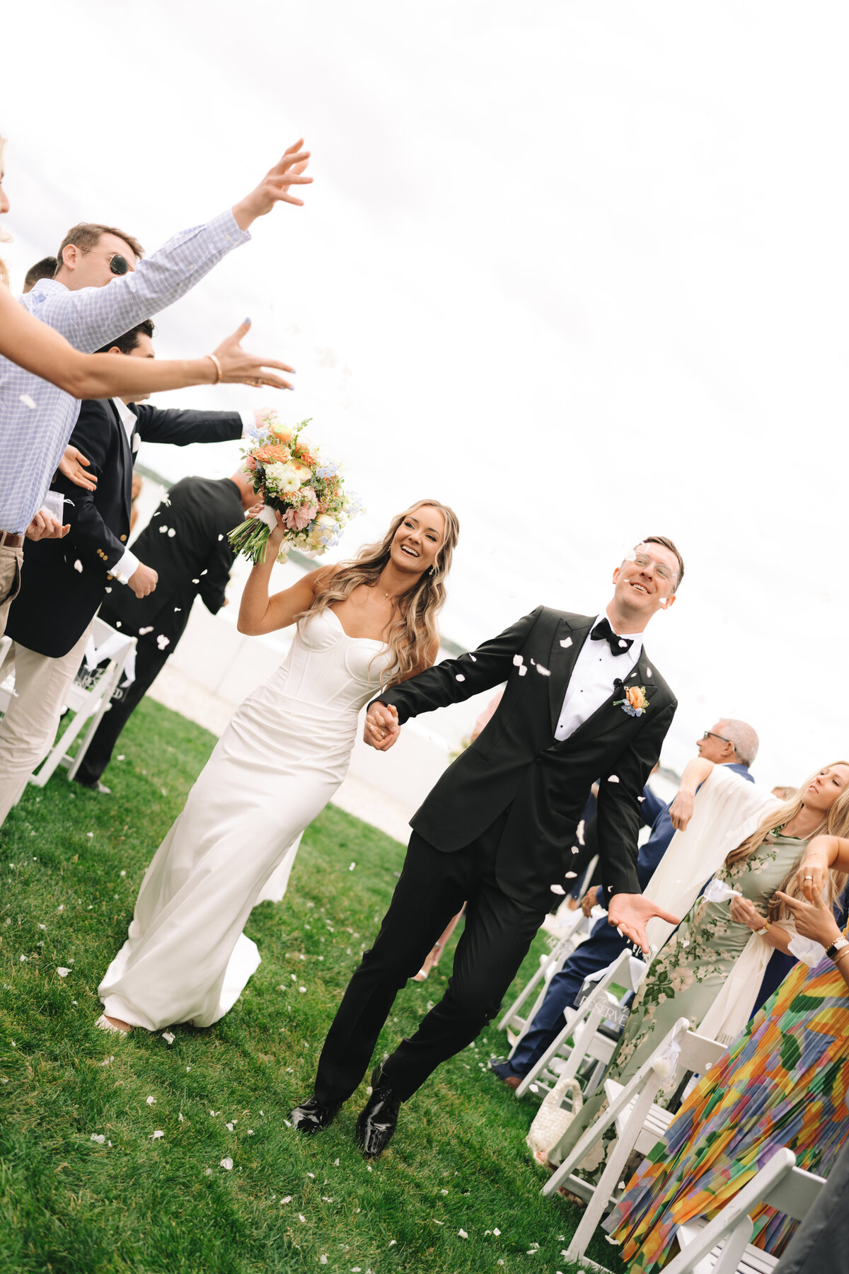 A bride and a groom at their Newport wedding ceremony walking down the aisle while their guest throw flower petals at them. 