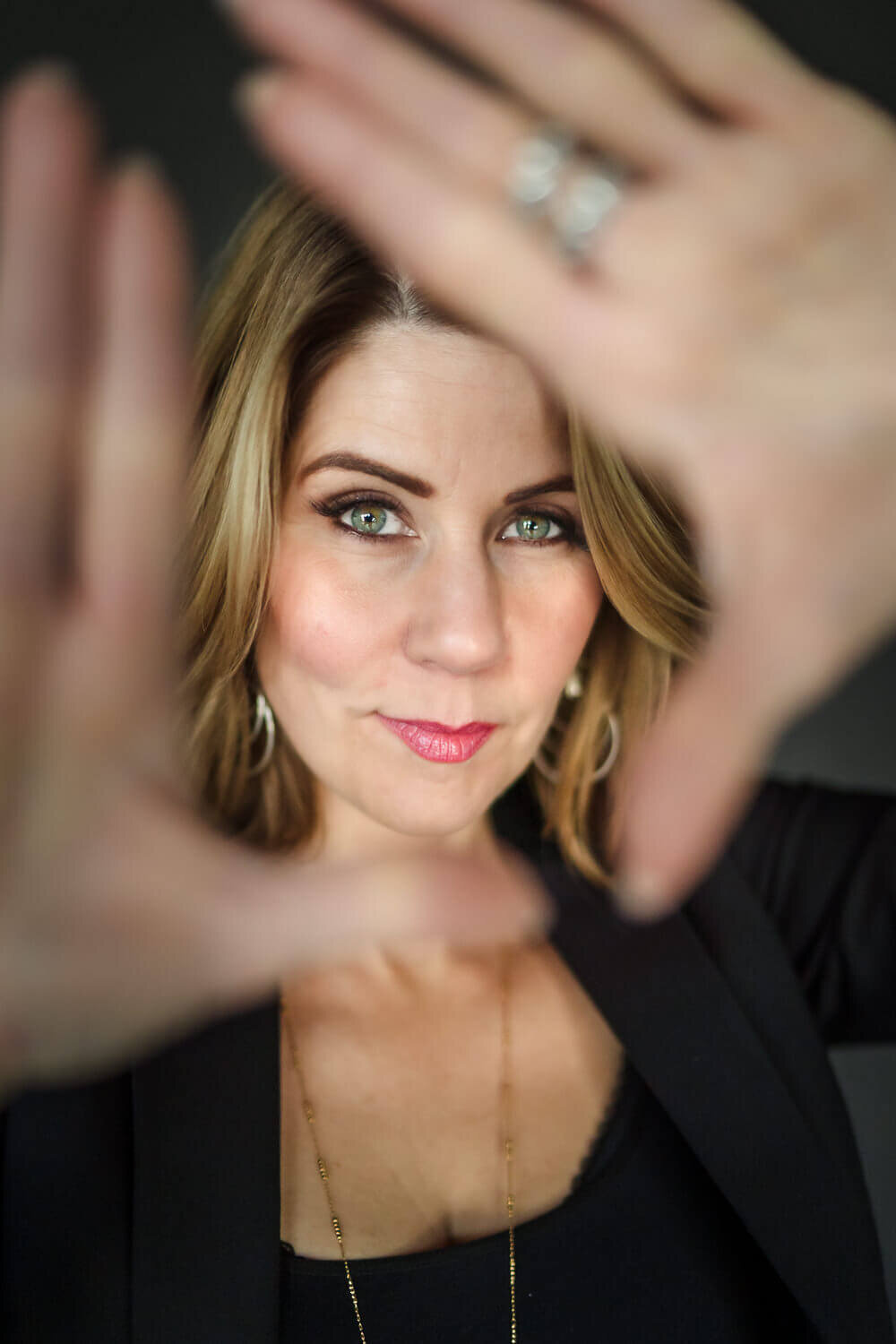 Woman with soft smile in black blazer holding both hands out of focus up to the camera 