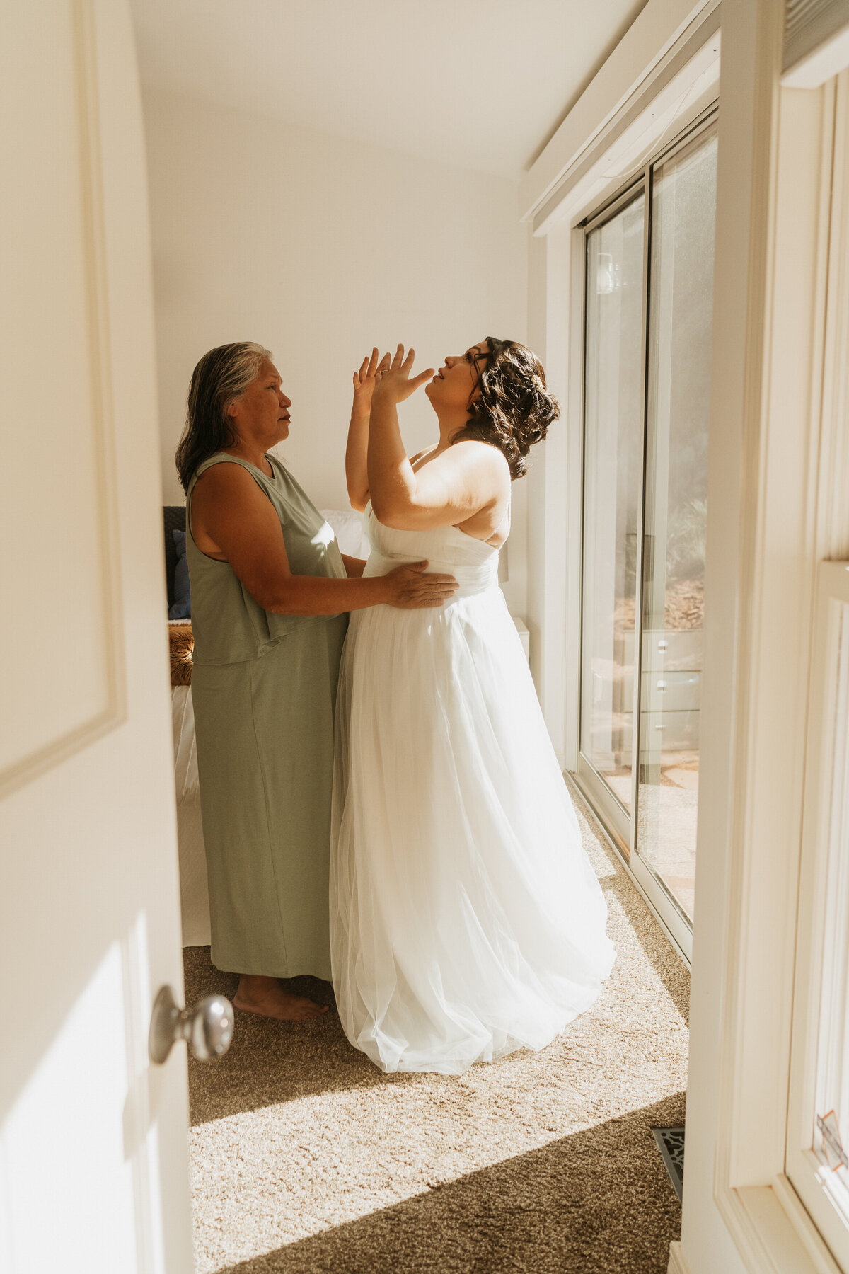 A person in a wedding dress laughing while a guest has their arms around their waist 