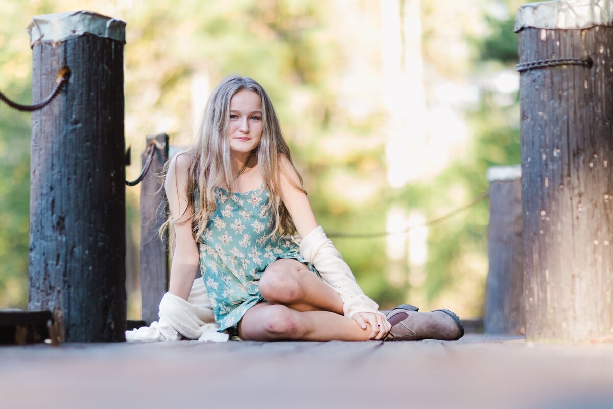 A girl sitting casually on a dock for her senior portrait.
