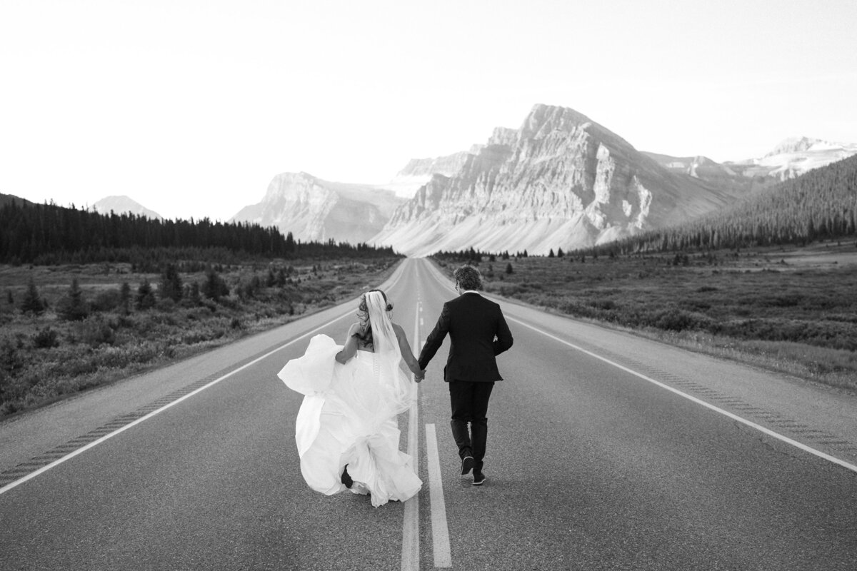 Couple holds hands and runs down road during Banff elopement