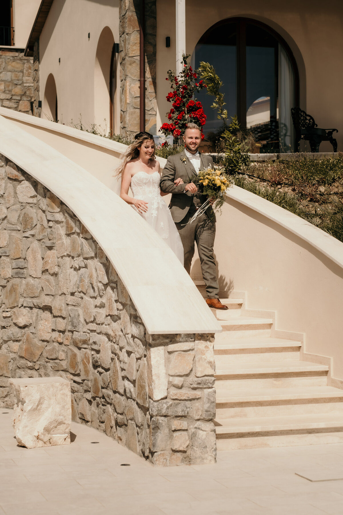 Das Hochzeitspaar läuft gemeinsam lächelnd eine geschwungene Steintreppe hinab.