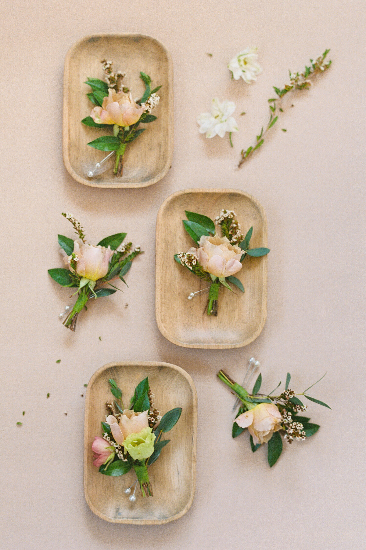 Flatlay of peach and ivory boutonnières with greenery and floral accents, styled for a Castle Ladyhawke wedding.