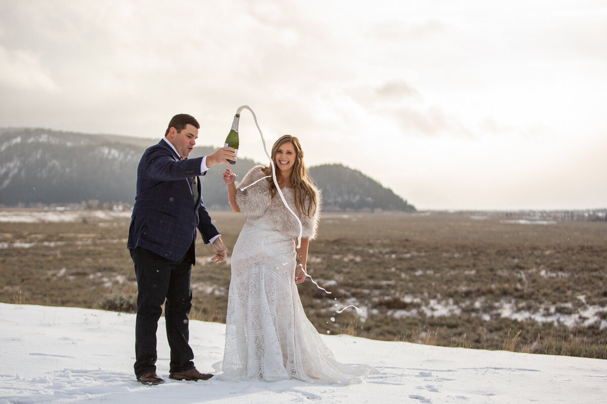 A groom pops champagne as his bride stands next to him cheering.