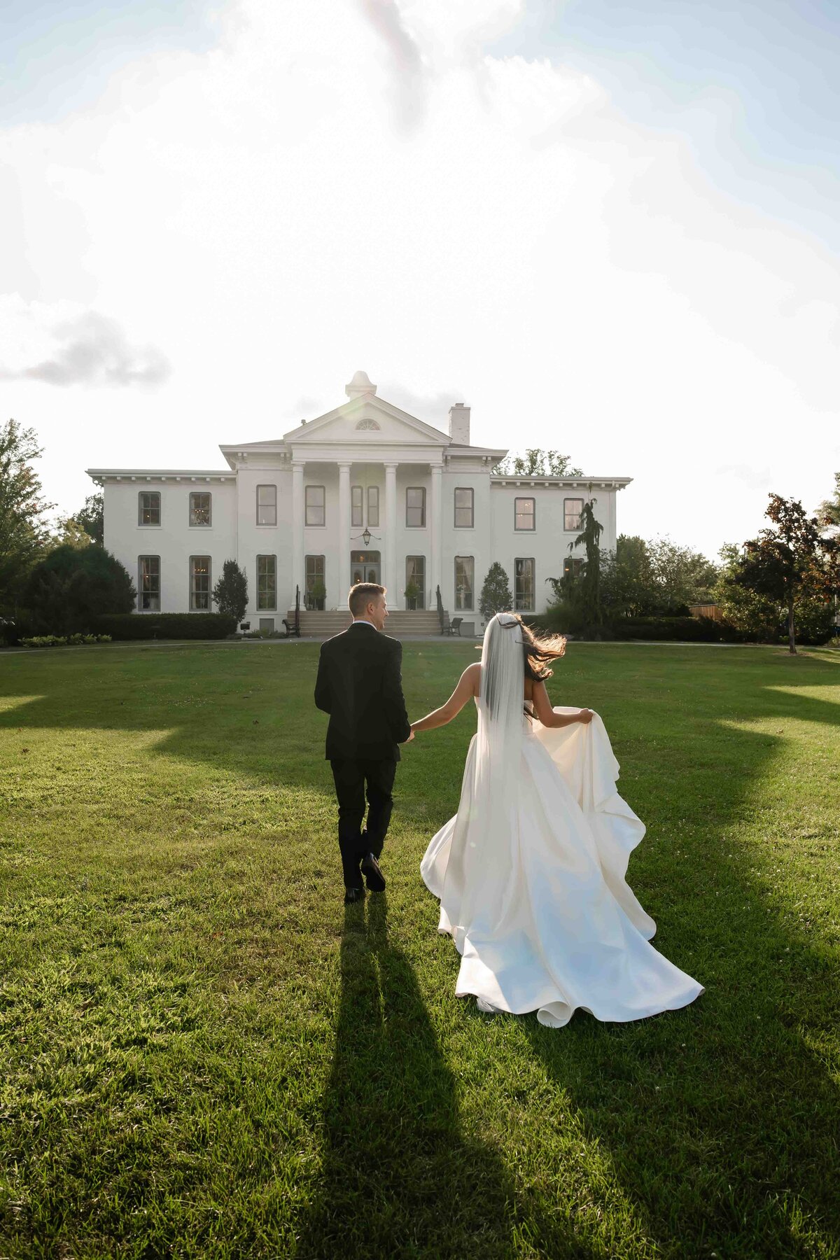 Bride and groom run towards white mansion at Wilder Mansion