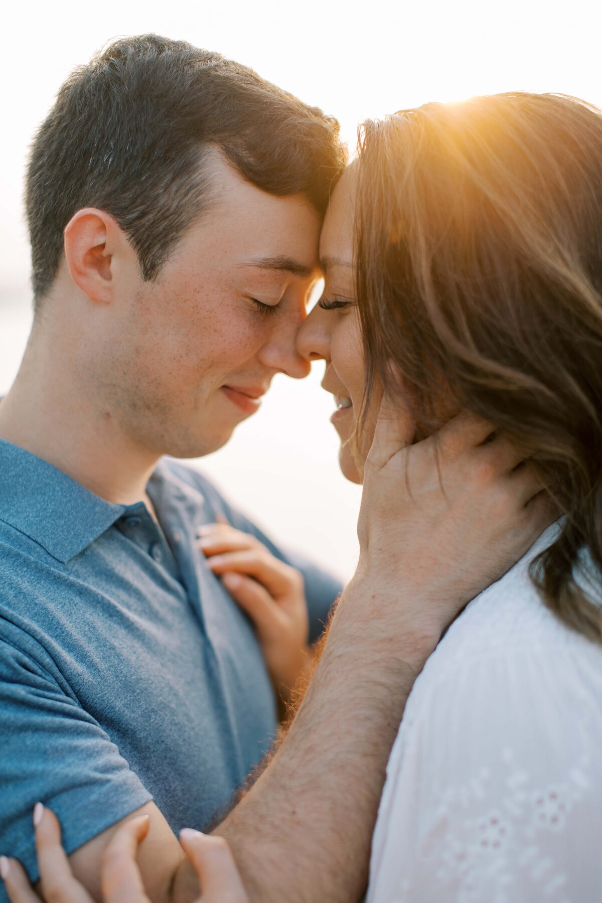Man and woman touching foreheads with their eyes closed with the sunlight peeking through behind them