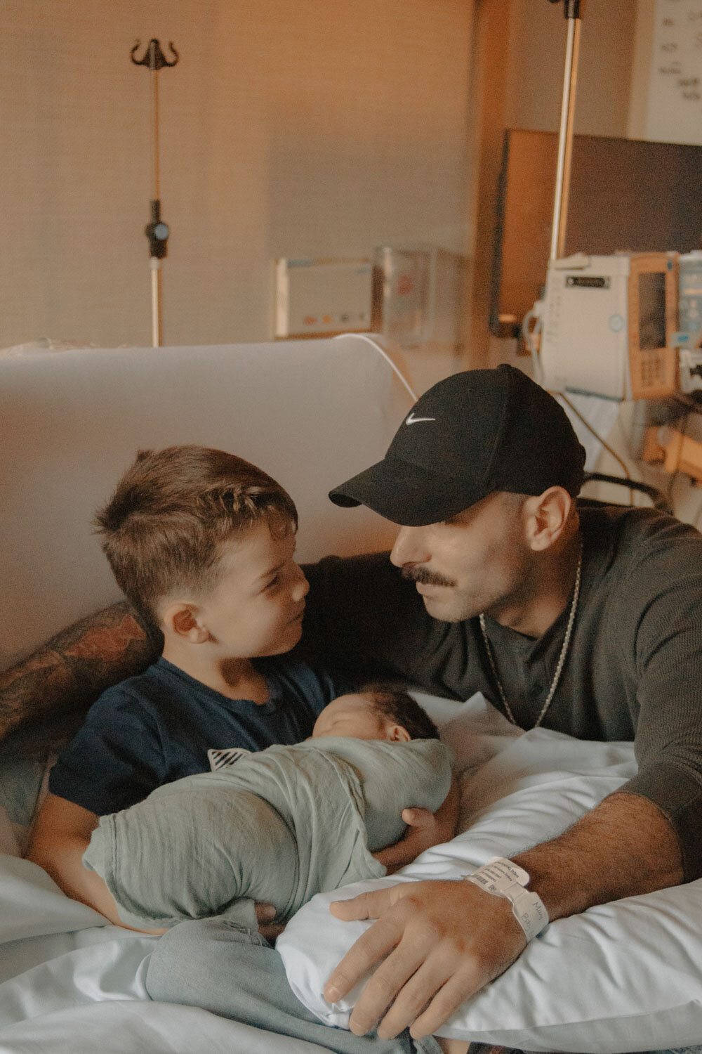 Father, son, and newborn sharing a moment in the hospital bed, with a calm and intimate atmosphere