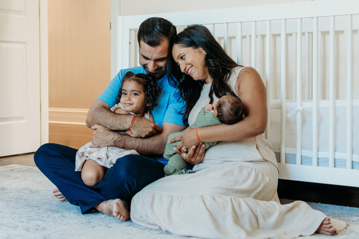 Family cuddles in front of the crib during a newborn family photoshoot in Northbrook, IL