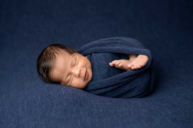 Newborn baby swaddled in navy wrap sleeping peacefully during Houston newborn photography session.